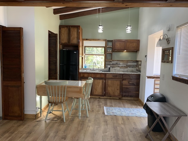 kitchen featuring sink, black fridge, lofted ceiling with beams, decorative light fixtures, and light wood-type flooring