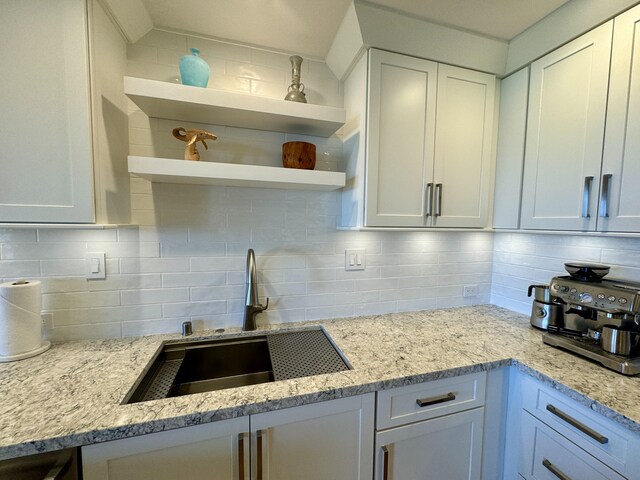 kitchen with light stone countertops, backsplash, white cabinets, and sink