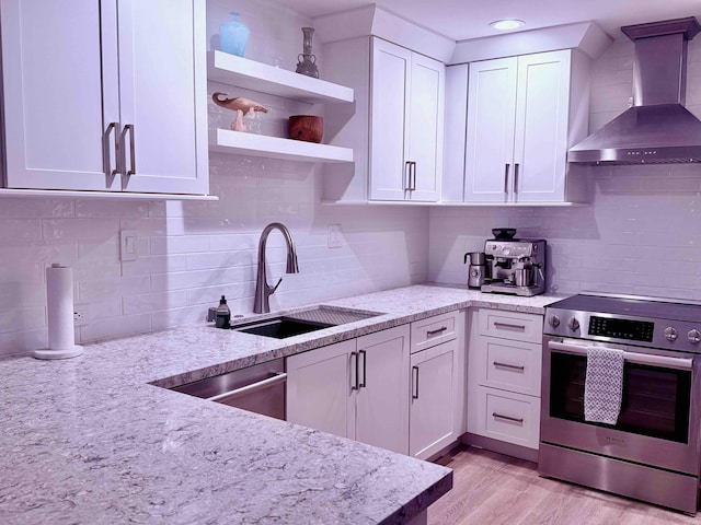 kitchen featuring white cabinetry, stainless steel appliances, wall chimney range hood, light stone counters, and light hardwood / wood-style floors