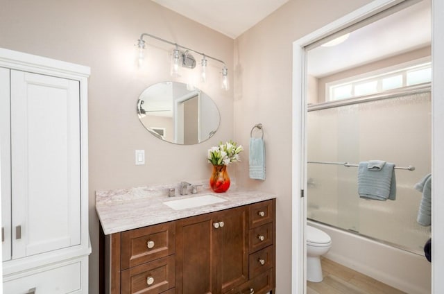 full bathroom with shower / bath combination with glass door, hardwood / wood-style floors, vanity, and toilet