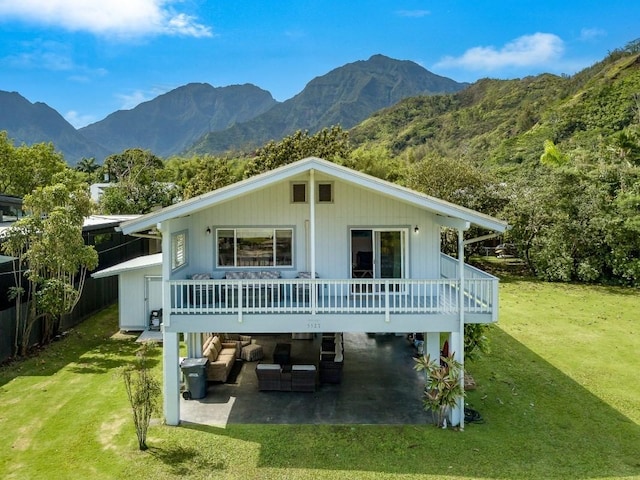 rear view of property with a lawn, a deck with mountain view, a patio, and an outdoor hangout area