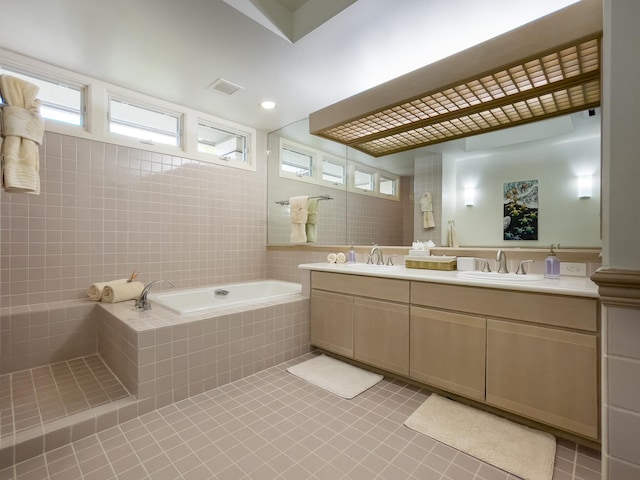 bathroom with tile patterned flooring, tile walls, tiled tub, and vanity