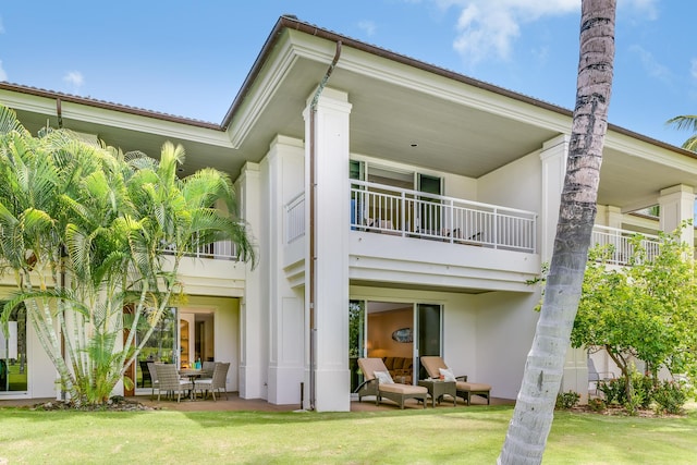 rear view of property featuring a yard, a balcony, and a patio