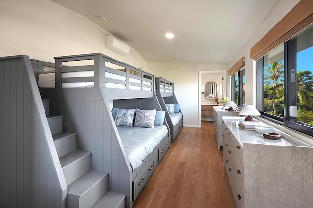 bedroom featuring ensuite bathroom, light hardwood / wood-style floors, lofted ceiling, and a wall unit AC