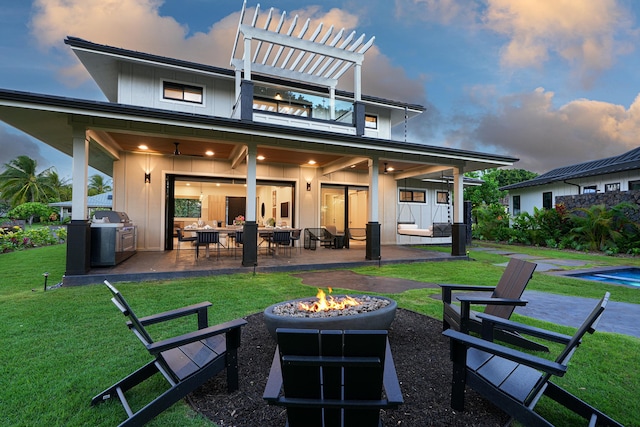 back house at dusk with a fire pit, a pergola, ceiling fan, area for grilling, and a patio