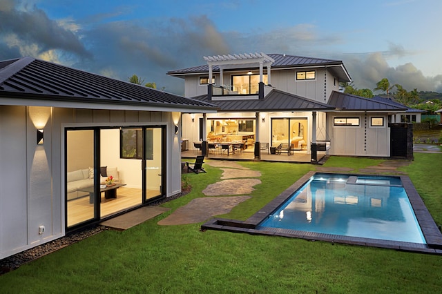 back house at dusk with a pergola, a balcony, a patio, outdoor lounge area, and a yard