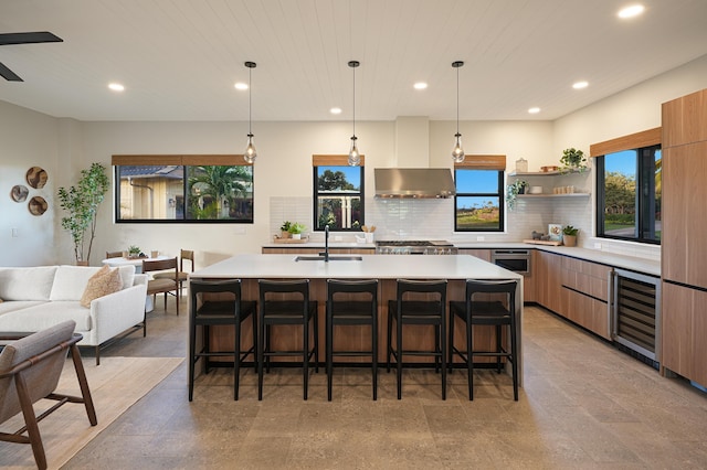 kitchen with a center island with sink, beverage cooler, wall chimney range hood, and sink