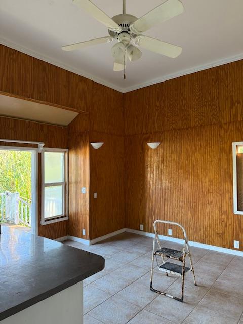 interior space featuring ceiling fan, wood walls, and crown molding