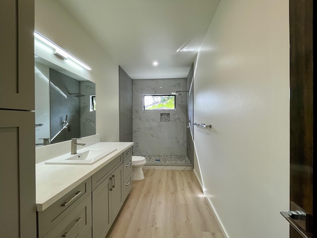 bathroom featuring a tile shower, toilet, vanity, and hardwood / wood-style flooring