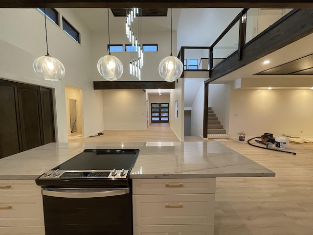 kitchen featuring stainless steel electric range, light stone countertops, white cabinetry, and a high ceiling