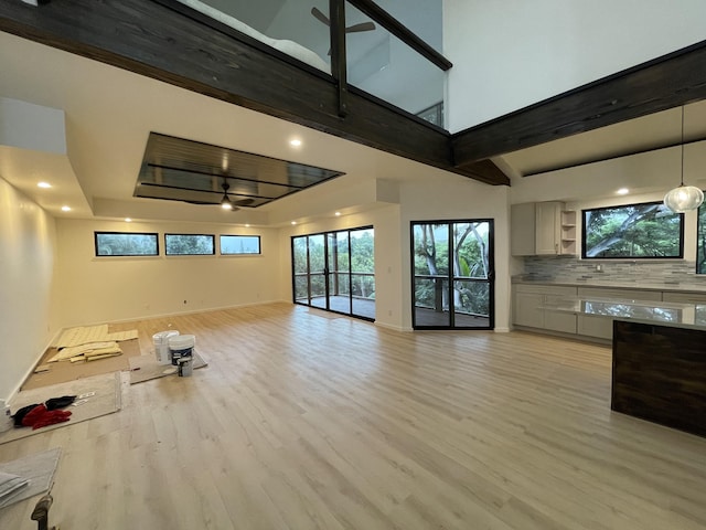 unfurnished living room featuring ceiling fan, light hardwood / wood-style flooring, and a towering ceiling