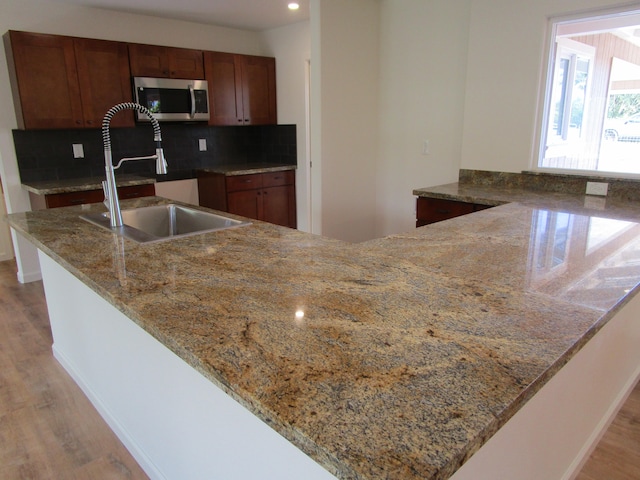 kitchen with backsplash, sink, light stone countertops, light hardwood / wood-style floors, and kitchen peninsula