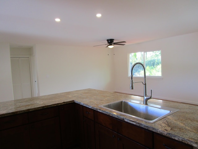 kitchen with ceiling fan, sink, light stone countertops, and dark brown cabinets