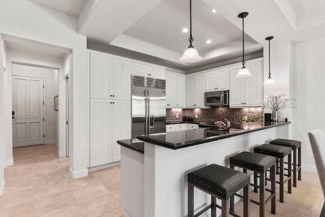 kitchen with a tray ceiling, white cabinetry, stainless steel appliances, and decorative light fixtures