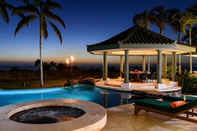 pool at dusk featuring a gazebo, a patio area, and an in ground hot tub