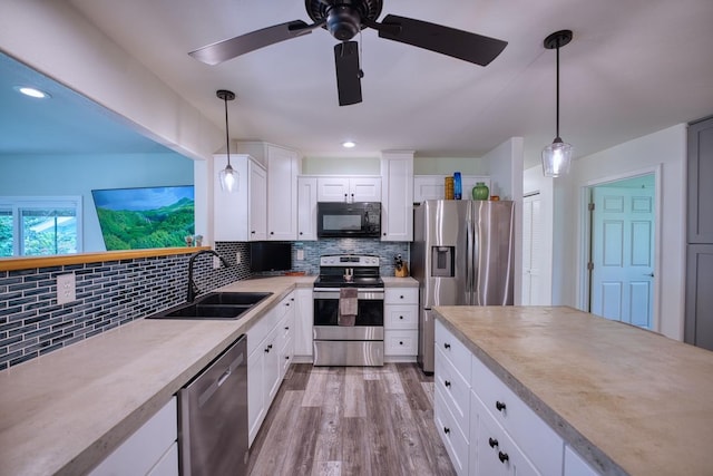 kitchen with appliances with stainless steel finishes, light wood-type flooring, sink, white cabinets, and hanging light fixtures