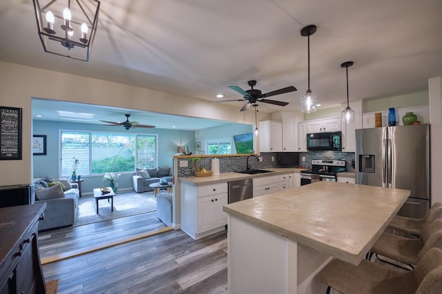 kitchen with a kitchen bar, hardwood / wood-style floors, white cabinets, and appliances with stainless steel finishes