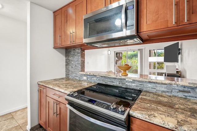 kitchen with decorative backsplash, appliances with stainless steel finishes, light tile patterned floors, and light stone countertops