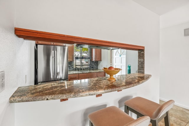 kitchen featuring stainless steel refrigerator, sink, kitchen peninsula, decorative backsplash, and light tile patterned floors