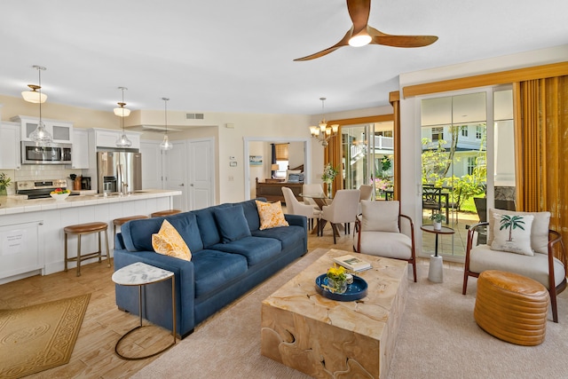 living room featuring ceiling fan with notable chandelier and light wood-type flooring