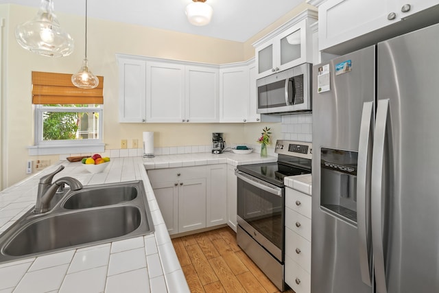 kitchen featuring white cabinetry, sink, tile counters, stainless steel appliances, and light hardwood / wood-style floors