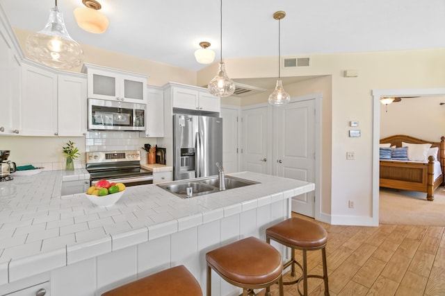 kitchen with kitchen peninsula, stainless steel appliances, sink, decorative light fixtures, and white cabinetry