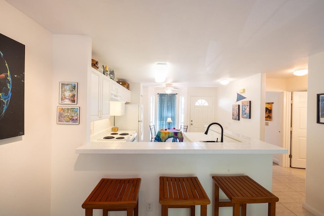 kitchen with kitchen peninsula, sink, ceiling fan, white fridge, and white cabinetry