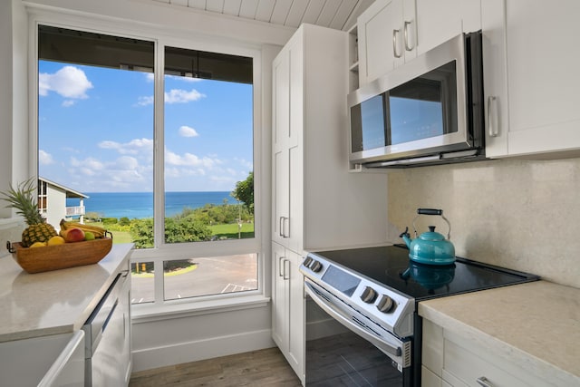 kitchen with a water view, decorative backsplash, light wood-type flooring, appliances with stainless steel finishes, and white cabinetry