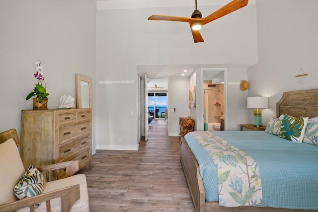 bedroom featuring ceiling fan, light wood-type flooring, a high ceiling, and connected bathroom