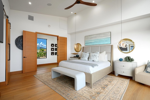 bedroom featuring ceiling fan, a barn door, wood-type flooring, and high vaulted ceiling