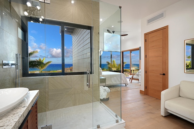 bathroom with an enclosed shower, vanity, ceiling fan, wood-type flooring, and a water view