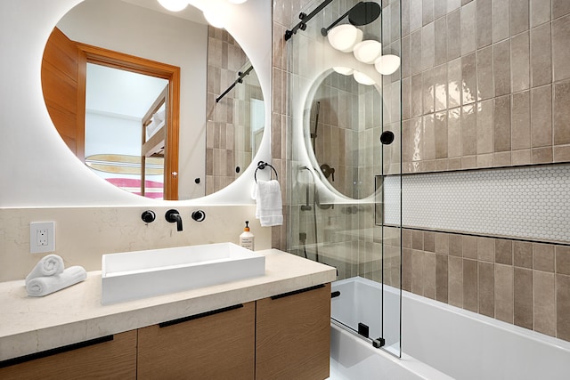 bathroom featuring vanity, combined bath / shower with glass door, and decorative backsplash