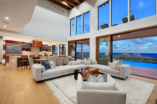 living room with beamed ceiling, a water view, a high ceiling, and light wood-type flooring