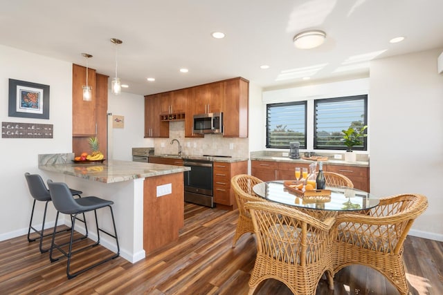 kitchen featuring kitchen peninsula, appliances with stainless steel finishes, tasteful backsplash, decorative light fixtures, and a breakfast bar