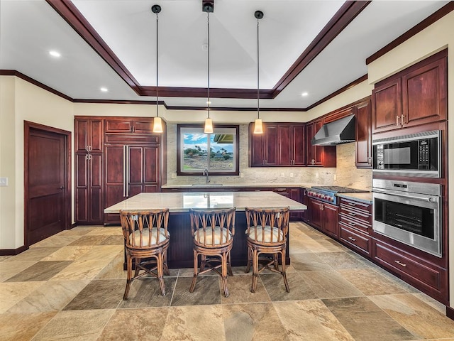 kitchen featuring decorative light fixtures, a kitchen island, sink, built in appliances, and wall chimney exhaust hood