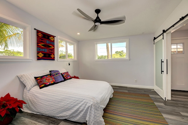 bedroom featuring ceiling fan, a barn door, and dark wood-type flooring