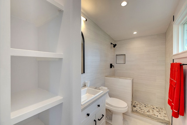 bathroom featuring tiled shower, vanity, toilet, and tile walls