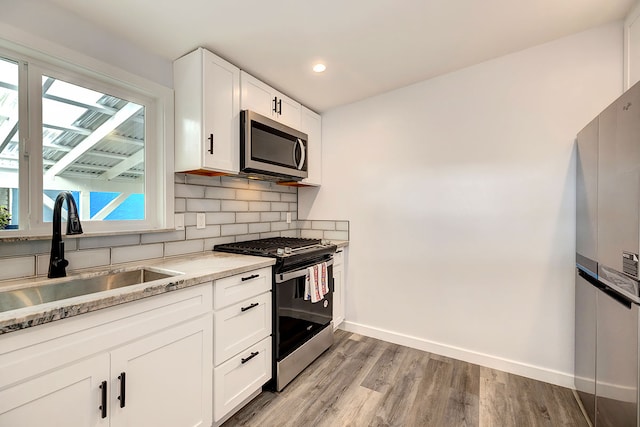 kitchen with sink, light hardwood / wood-style floors, light stone counters, white cabinetry, and stainless steel appliances