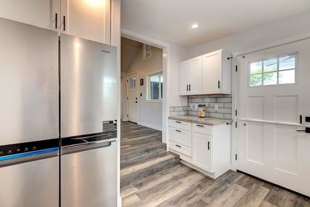 kitchen featuring stainless steel fridge, white cabinets, light stone counters, and light hardwood / wood-style floors