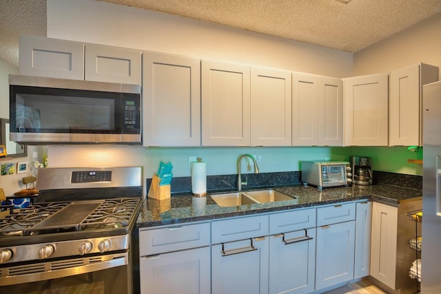 kitchen with stainless steel appliances, dark stone countertops, a textured ceiling, white cabinets, and sink