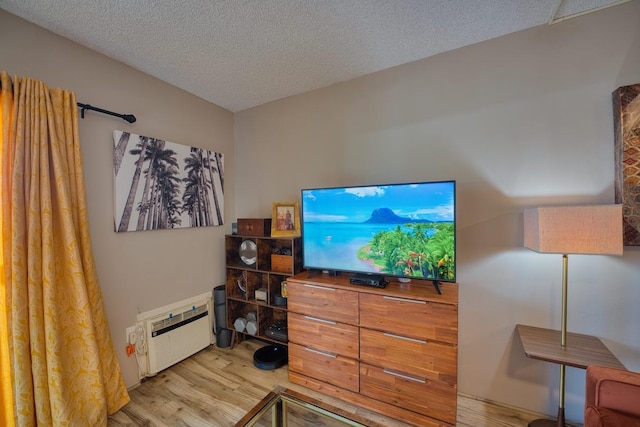 bedroom with a textured ceiling, light hardwood / wood-style flooring, and an AC wall unit