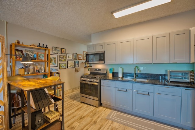 kitchen with a textured ceiling, stainless steel appliances, dark stone countertops, light hardwood / wood-style floors, and sink