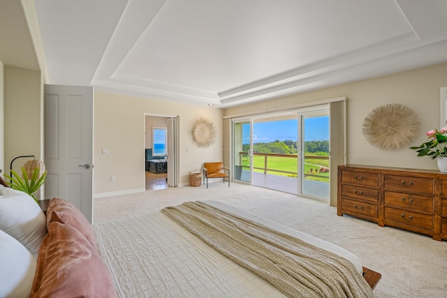 carpeted bedroom with a raised ceiling, ensuite bathroom, and access to exterior