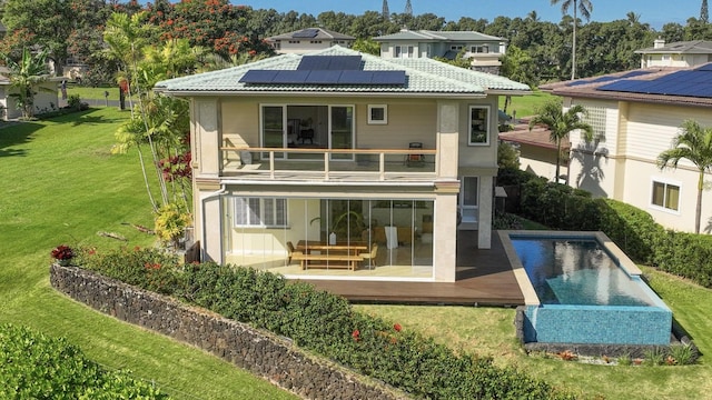 rear view of property with a lawn, a patio area, a balcony, and solar panels