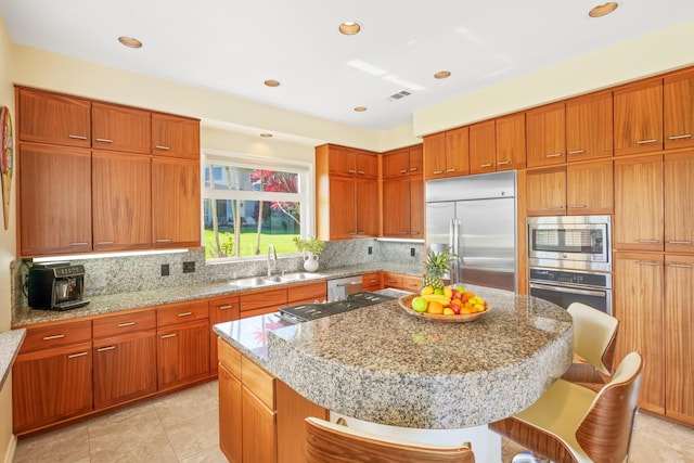 kitchen with a kitchen breakfast bar, tasteful backsplash, sink, built in appliances, and a kitchen island