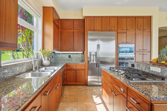 kitchen with backsplash, light stone counters, sink, light tile patterned floors, and built in appliances