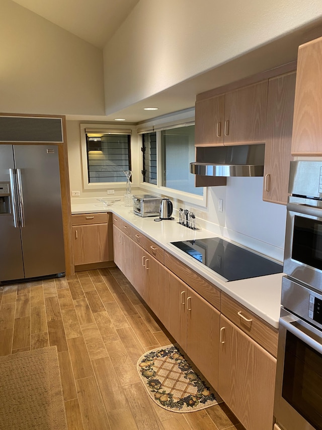 kitchen with light brown cabinets, appliances with stainless steel finishes, ventilation hood, and a towering ceiling