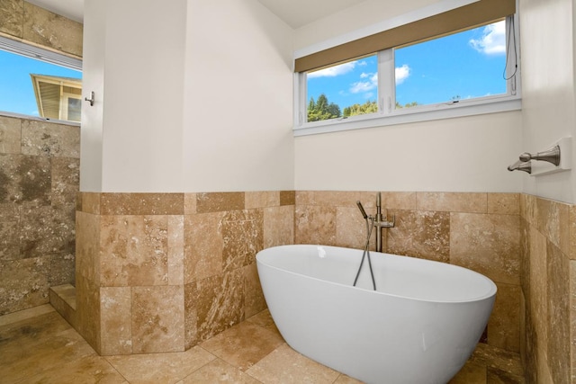 bathroom with a bath, plenty of natural light, and tile walls