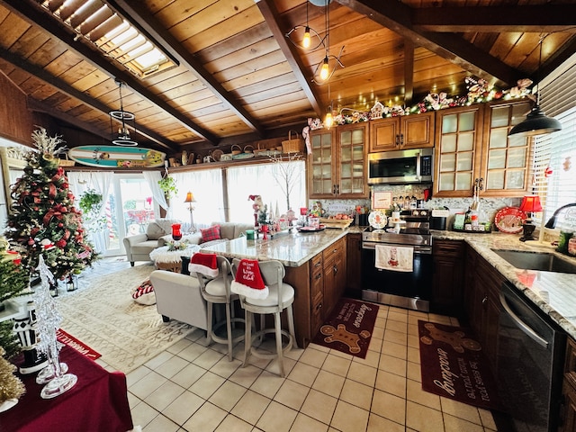 kitchen with sink, vaulted ceiling with beams, light stone counters, pendant lighting, and appliances with stainless steel finishes