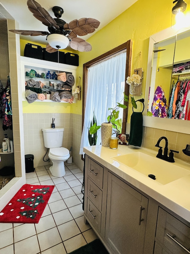 bathroom with ceiling fan, tile patterned flooring, toilet, vanity, and tile walls